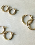 A set of four pairs of Becoming Jewelry's Everyday Hoop Earrings in classic gold, varying sizes, and perfect as lightweight accessories for any day, elegantly displayed against a light beige surface.