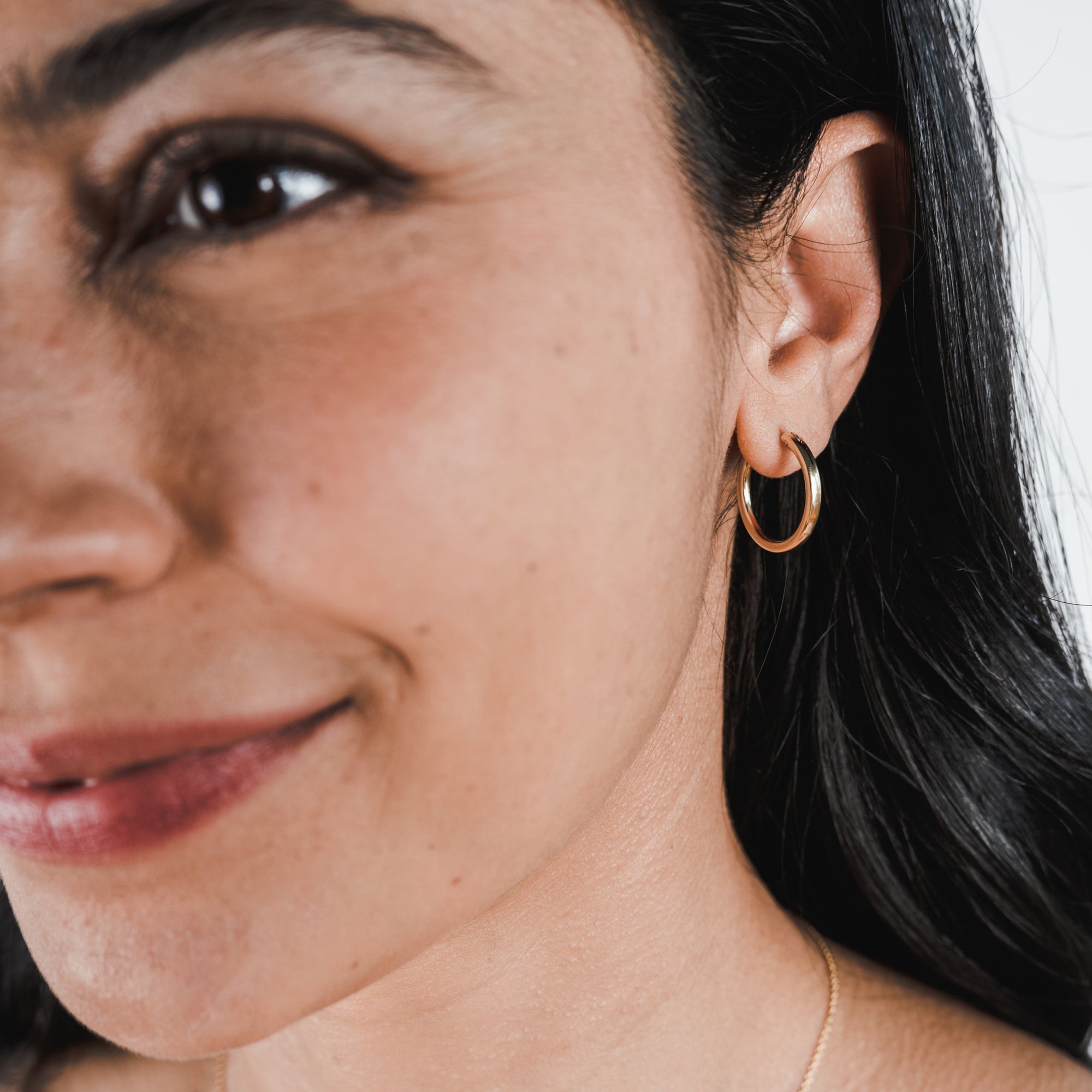 Close-up of a smiling woman with Becoming Jewelry Gold Filled Everyday Hoop Earrings, large.