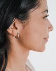 Profile view of a person with long dark hair, wearing a medium-sized, classic Everyday Hoop Earring by Becoming Jewelry in their left ear. The background is plain white.