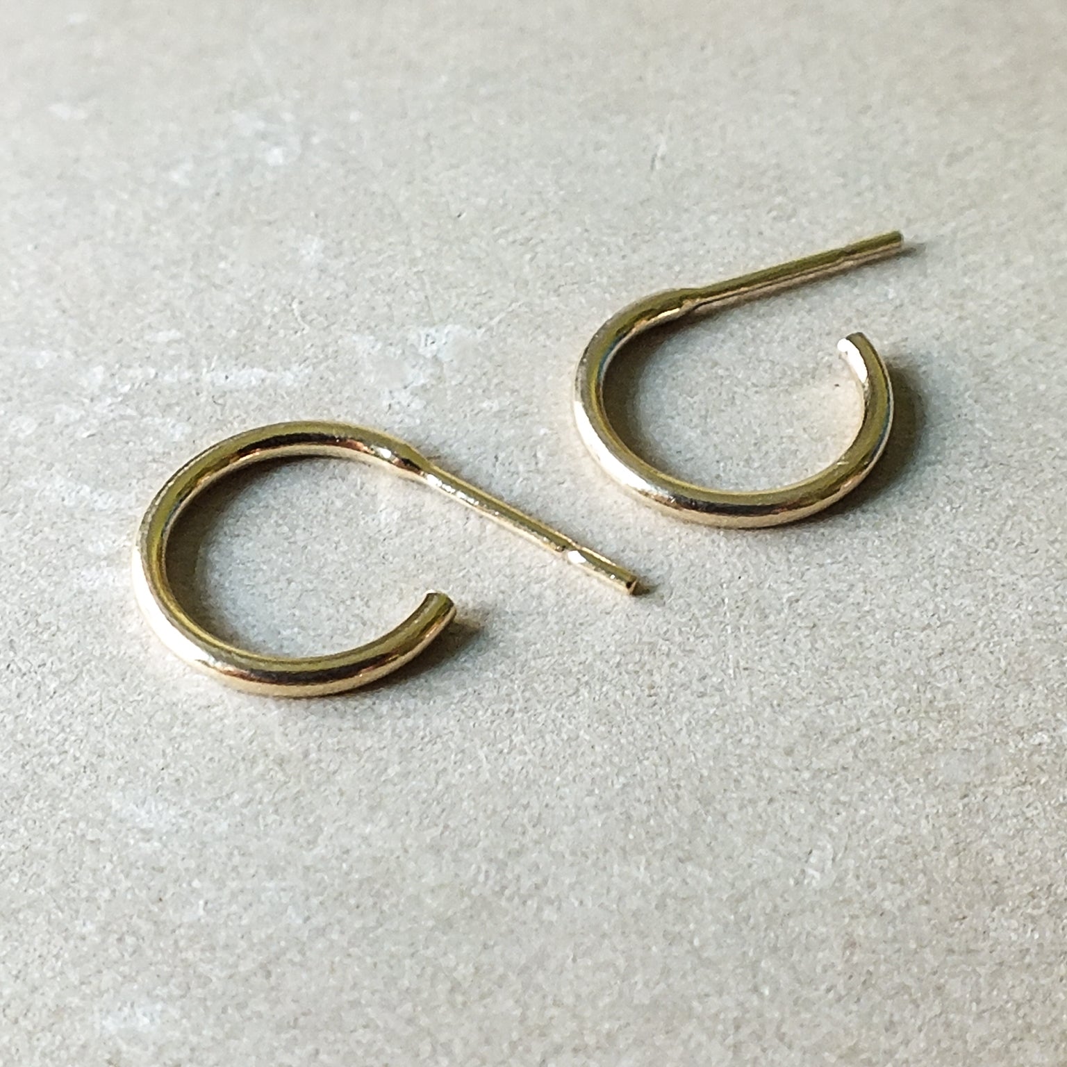 A pair of Open Hoop Earrings, small, by Becoming Jewelry, lays side by side on a beige surface.