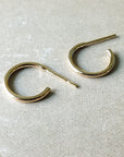 A pair of Open Hoop Earrings, small, by Becoming Jewelry, lays side by side on a beige surface.
