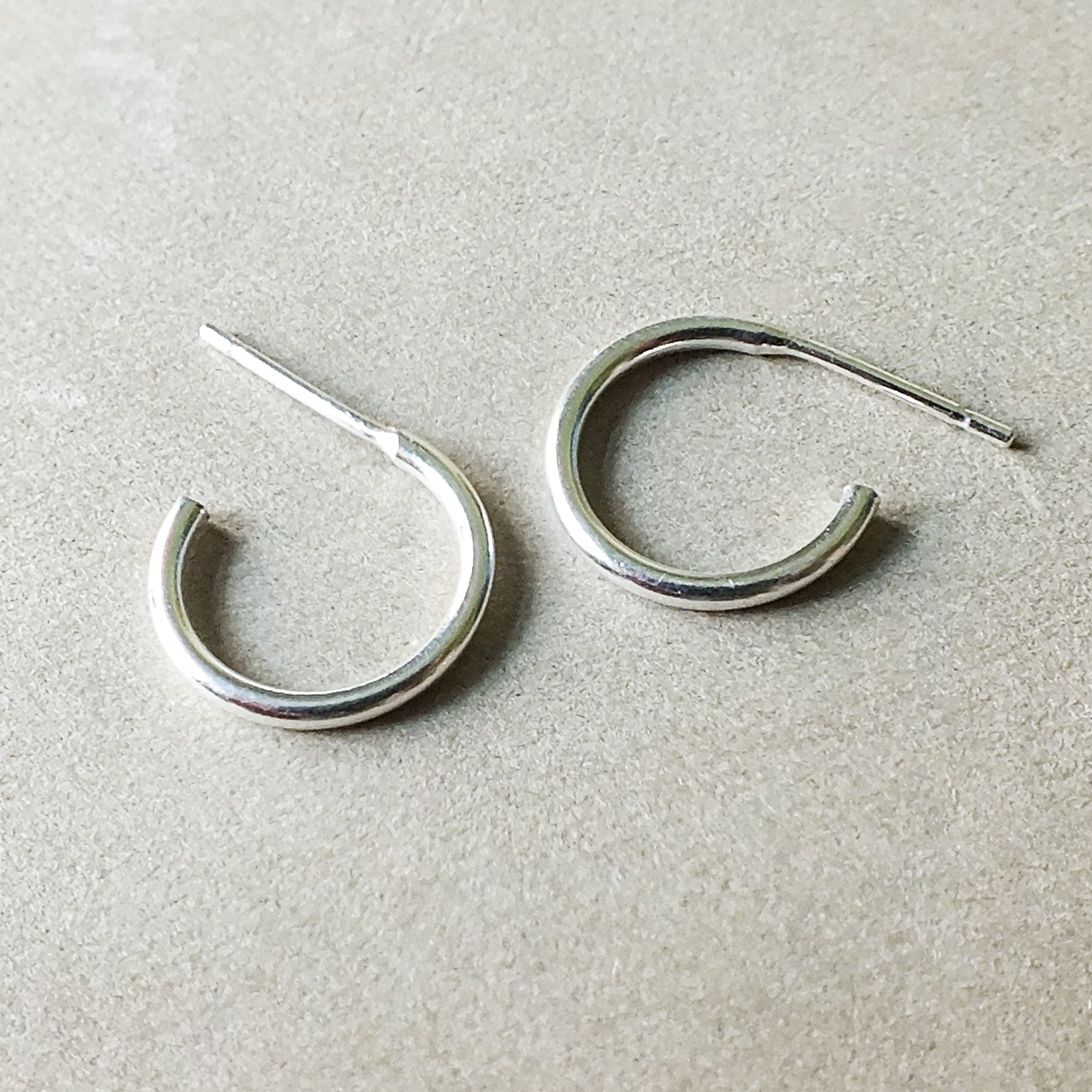 A pair of small Open Hoop Earrings from Becoming Jewelry with straight posts, resting on a textured surface.
