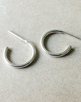 A pair of dainty, Becoming Jewelry Open Hoop Earrings, small on a beige surface.