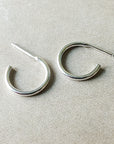 A pair of small Open Hoop Earrings from Becoming Jewelry with straight posts, resting on a textured surface.