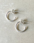A pair of silver Open Hoop Earrings, small by Becoming Jewelry, delicately placed on a neutral textured surface.
