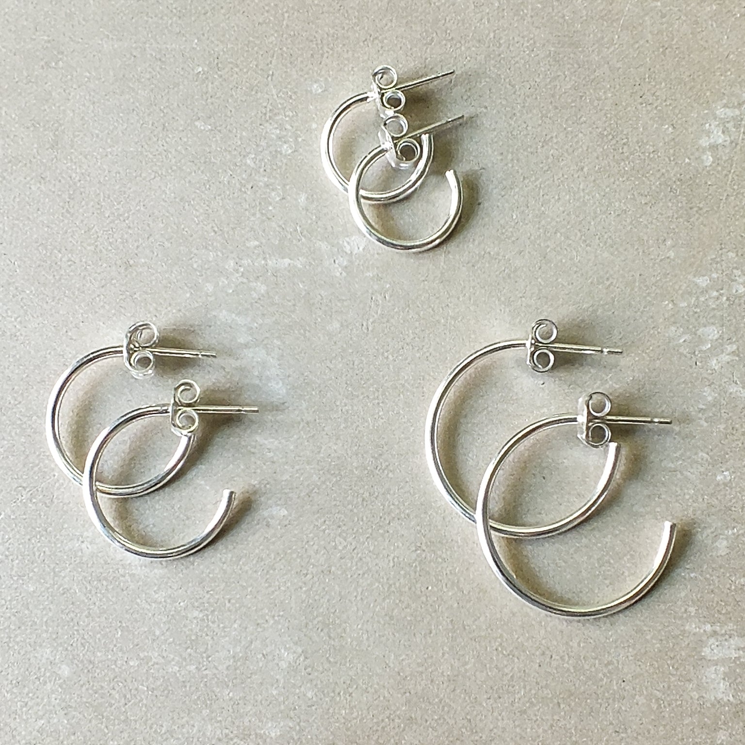 Four Becoming Jewelry small Open Hoop Earrings with a unique layered design on a gray background, crafted from sterling silver.