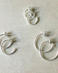 Four Becoming Jewelry small Open Hoop Earrings with a unique layered design on a gray background, crafted from sterling silver.