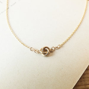 Love Knot Necklace by Becoming Jewelry with a knot pendant on a beige background.