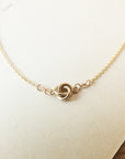 A delicate Love Knot Necklace by Becoming Jewelry, featuring a small gold knot pendant, is showcased on a light, off-white background, making it the perfect gift.