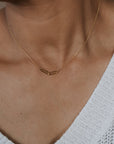 Necklace with geometric pendant on a person wearing a white sweater.