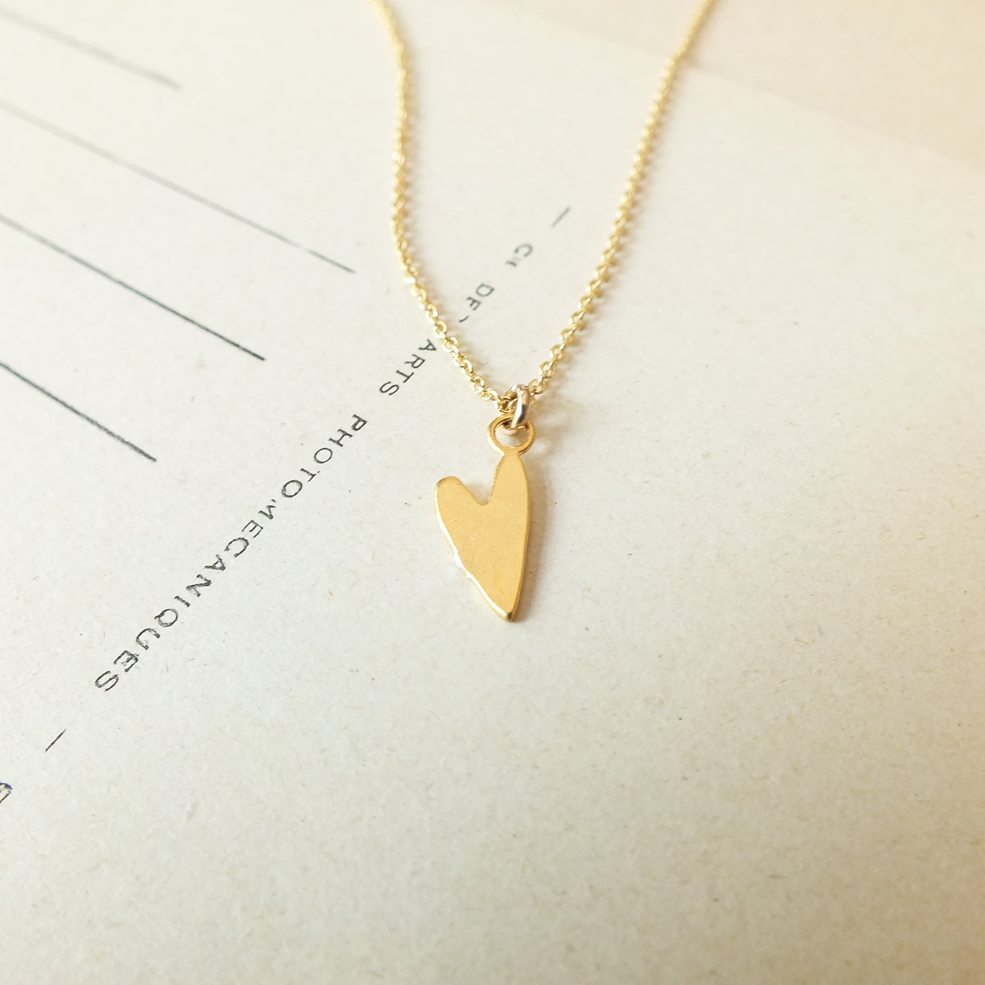 A gold Love Deeply Necklace from Becoming Jewelry, featuring a heart charm, rests on a white background accompanied by some text and lines.