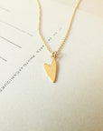 A gold Love Deeply Necklace from Becoming Jewelry, featuring a heart charm, rests on a white background accompanied by some text and lines.