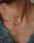 Necklace with a delicate pendant worn by a person in a textured garment.