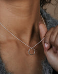 Person wearing a silver necklace with a small pendant, holding it near their neck.