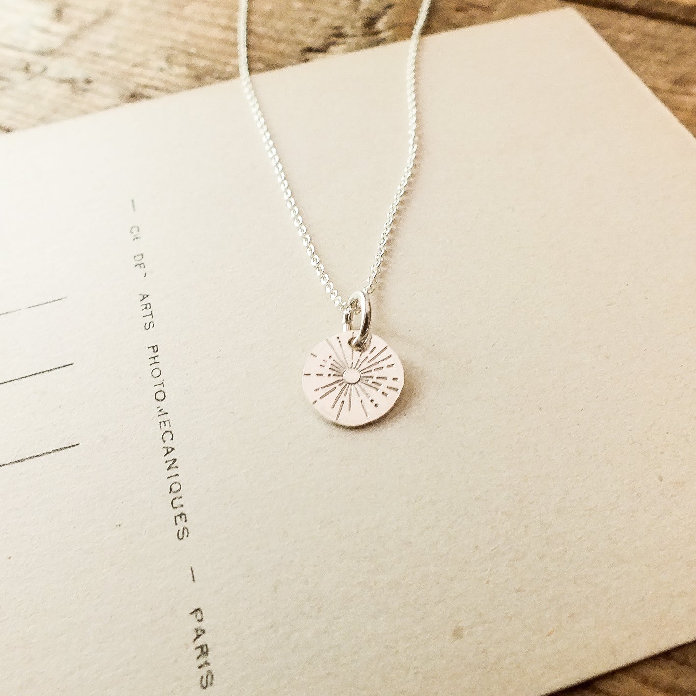Becoming Jewelry&#39;s Be The Light Necklace with Sunshine Charm design on a wooden surface.