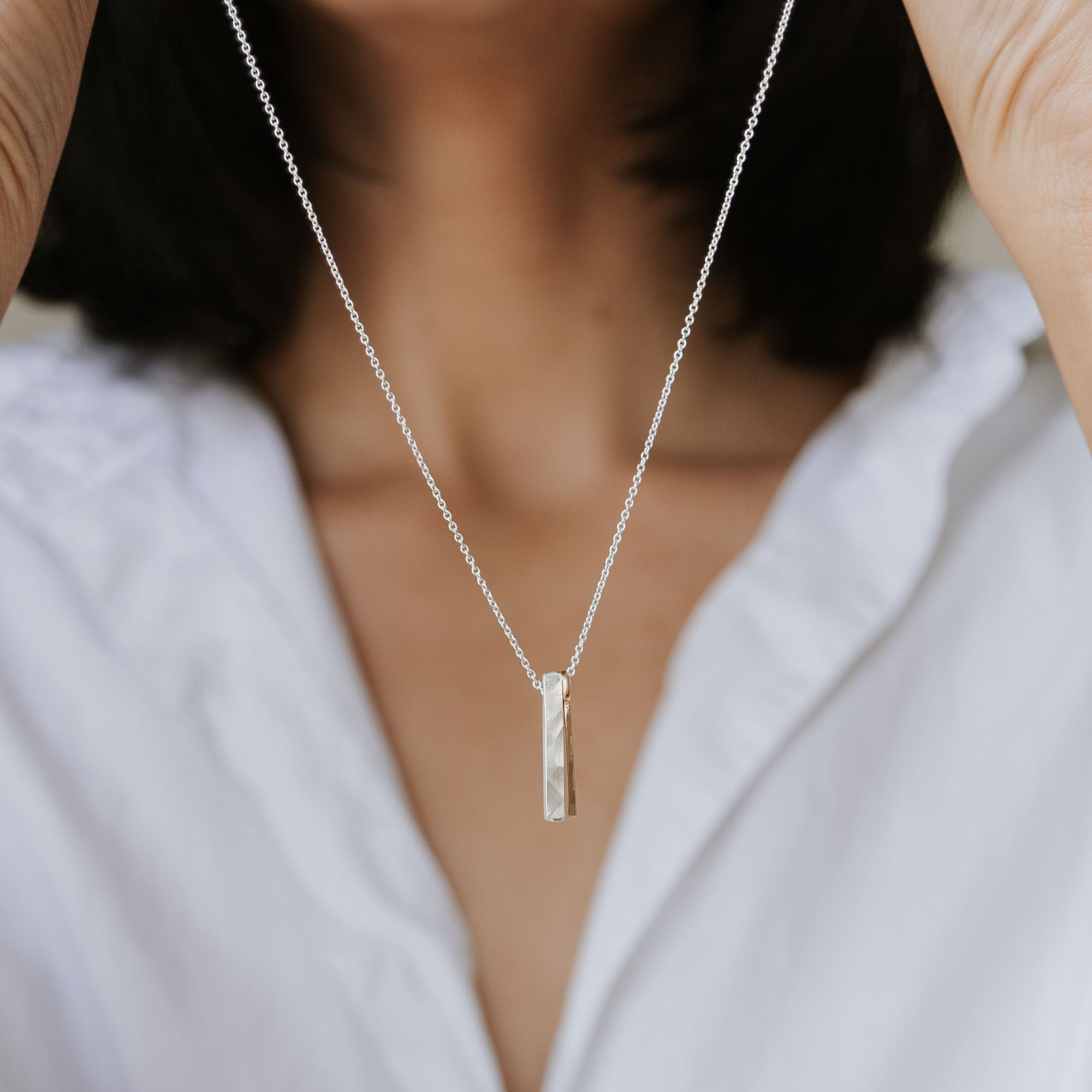 A person holds up the best-selling Through Thick & Thin Necklace from Becoming Jewelry, featuring a vertical rectangular pendant, showcasing it against a white shirt—a perfect gift symbolizing enduring connections.