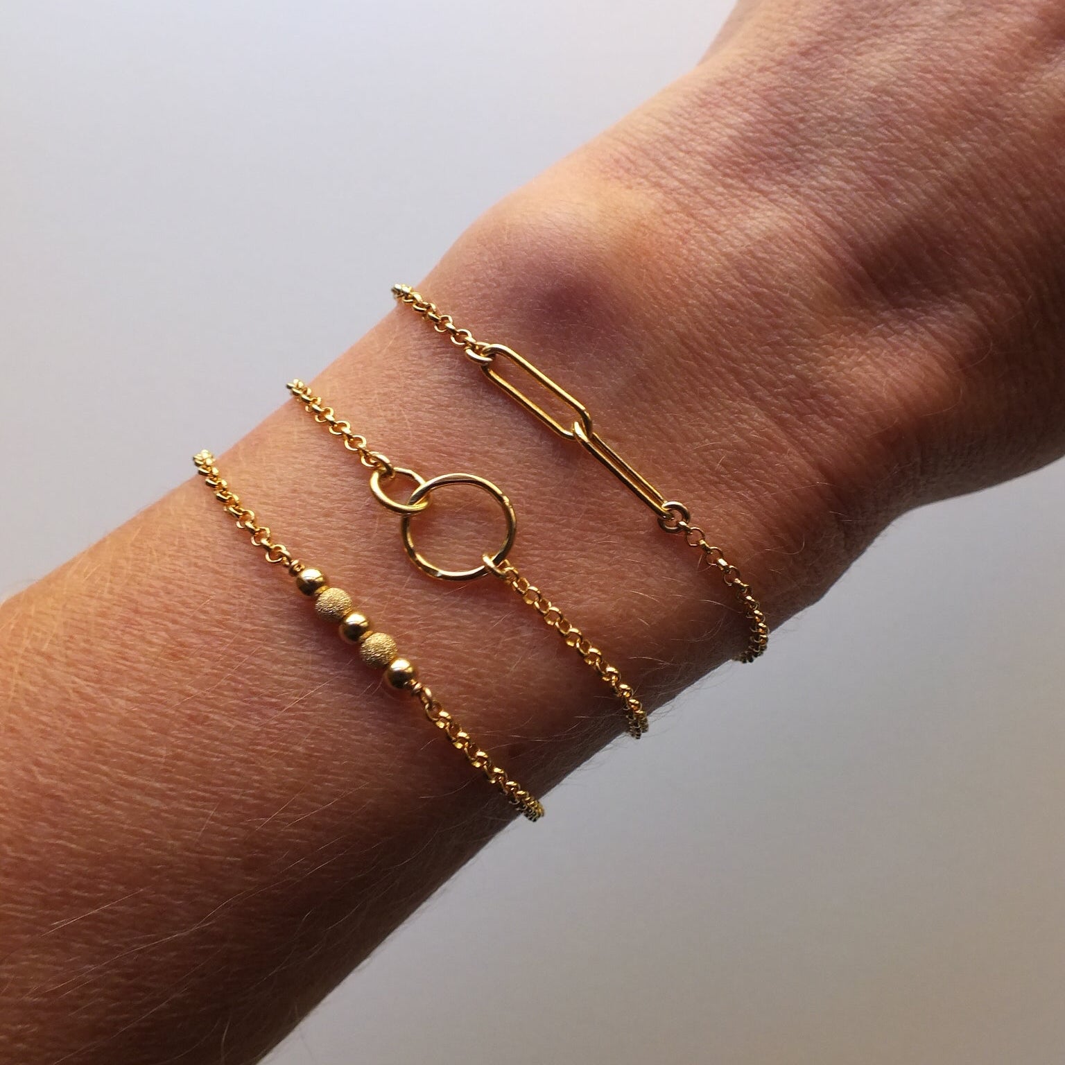 Gold bracelets on a wrist against a plain background