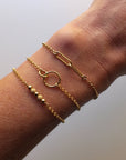 Gold bracelets on a wrist against a plain background