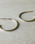 Two large open hoop earrings from Becoming Jewelry rest on a light beige surface.