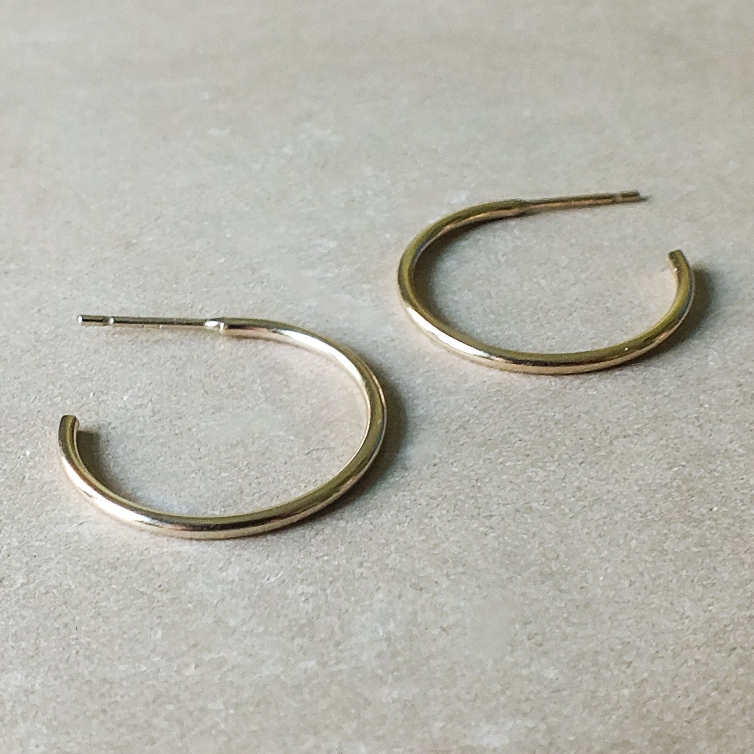 A pair of dainty large Becoming Jewelry open hoop earrings on a plain surface.