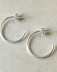 A pair of large, lightweight silver Open Hoop Earrings from Becoming Jewelry, laying on a beige surface, perfect for those who appreciate dainty jewelry.