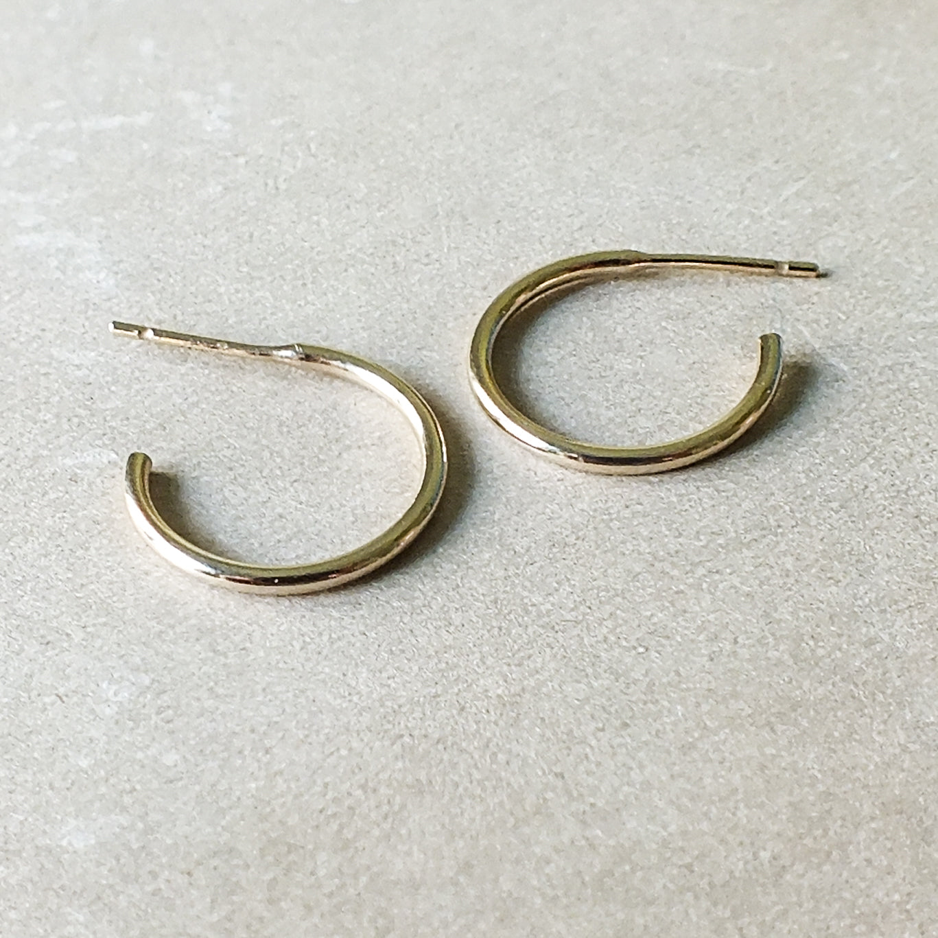 A pair of medium Open Hoop Earrings by Becoming Jewelry is displayed on a light beige surface, exuding a classic and dainty charm.