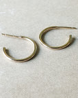 A pair of medium Open Hoop Earrings by Becoming Jewelry is displayed on a light beige surface, exuding a classic and dainty charm.