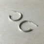 Two Becoming Jewelry medium Open Hoop Earrings in sterling silver on a gray surface.