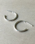 A pair of Open Hoop Earrings, medium from Becoming Jewelry, featuring a simple and classic silver design with open ends, are placed on a flat, light-colored surface. These dainty hoops are lightweight and perfect for everyday wear.