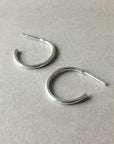 Two Becoming Jewelry medium Open Hoop Earrings in sterling silver on a gray surface.