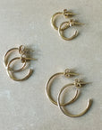 Three pairs of classic gold hoop earrings from Becoming Jewelry, including their Open Hoop Earrings in medium size, are displayed on a plain surface. These dainty hoops are lightweight, making them perfect for everyday wear.