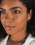 Close-up of a woman with curly hair wearing Becoming Jewelry's large Open Hoop Earrings, a dainty necklace, and a white top, looking slightly to the right.