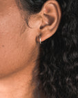 Close-up of a person's ear adorned with small Open Hoop Earrings by Becoming Jewelry. The person has a medium to dark skin tone and curly hair.