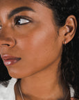 Side profile of a woman with curly hair, adorned with dainty Becoming Jewelry sterling silver open hoop earrings, small, looking away from the camera.