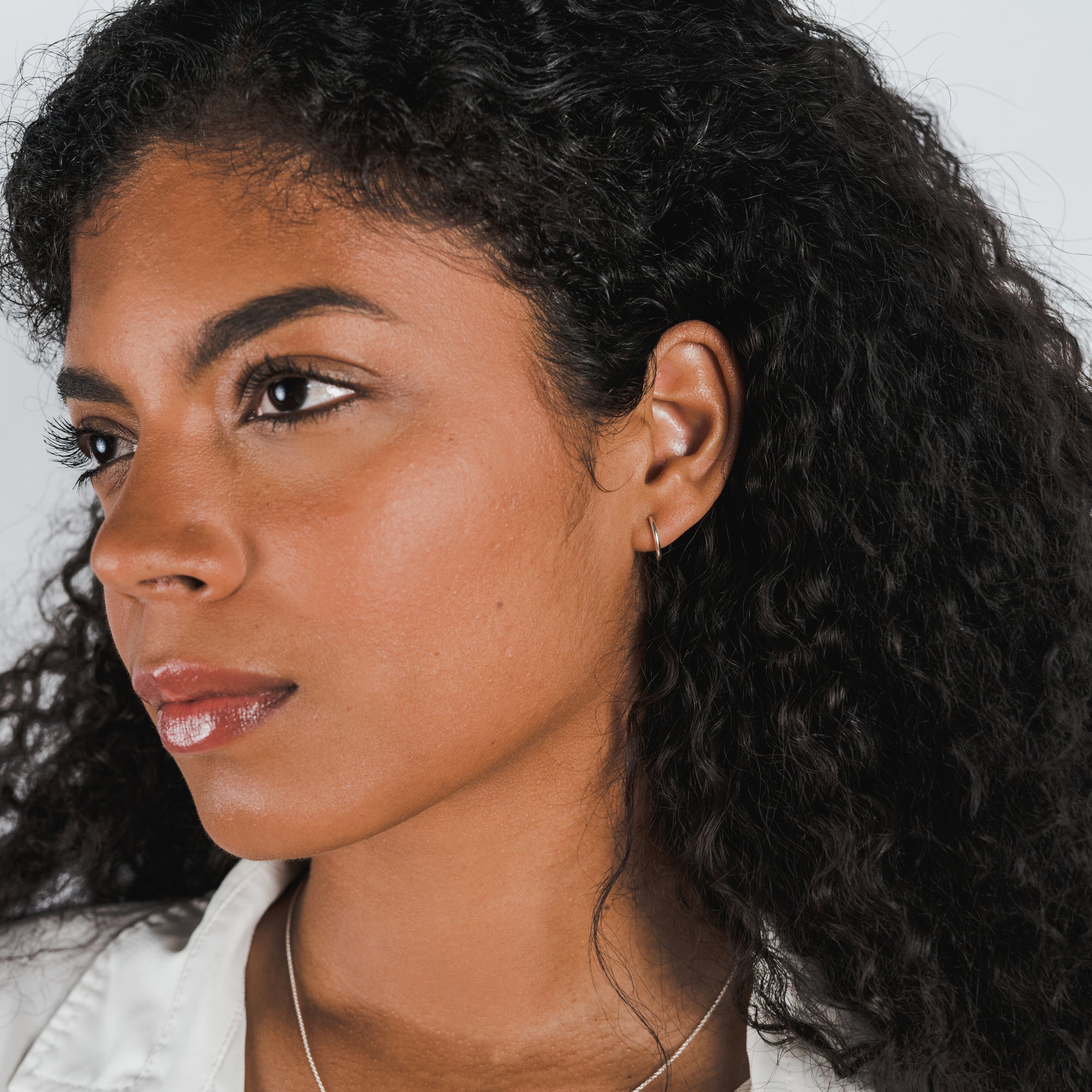 A woman with curly hair wearing Becoming Jewelry Open Hoop Earrings, small looks to the side against a white background.