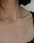 Close-up of a person wearing the Shine Necklace by Becoming Jewelry, featuring a delicate silver chain with a small, round pendant. The pendant is adorned with a sparkling Cubic Zirconia charm, perfectly complementing their brown sleeveless top.