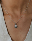 Necklace with a pendant worn by a person in a light-colored outfit
