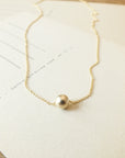 Simplify Necklace by Becoming Jewelry with a single bead displayed on a piece of paper.