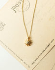 Gold necklace with a sun-shaped pendant on an old postcard background