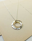 Necklace with a gold and silver circular pendant on a beige card.