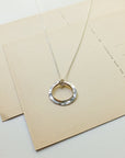 Silver necklace with a circular pendant on a beige envelope
