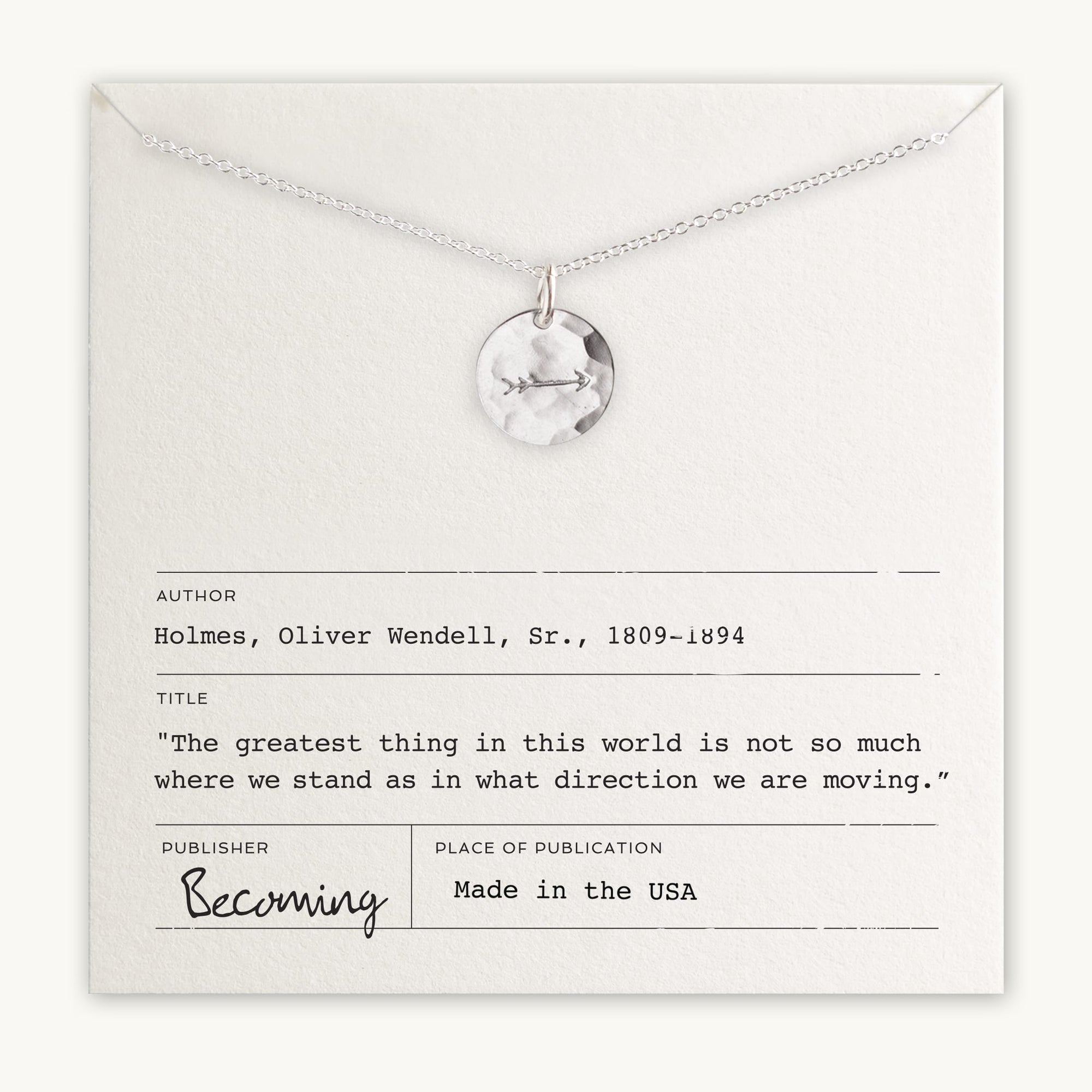 The Arrow Necklace, crafted by Becoming Jewelry, features a silver chain with a circular pendant and an arrow charm. It is presented on an off-white card adorned with an inspiring quote by Oliver Wendell Holmes, Sr., indicating that the product is made in the USA.
