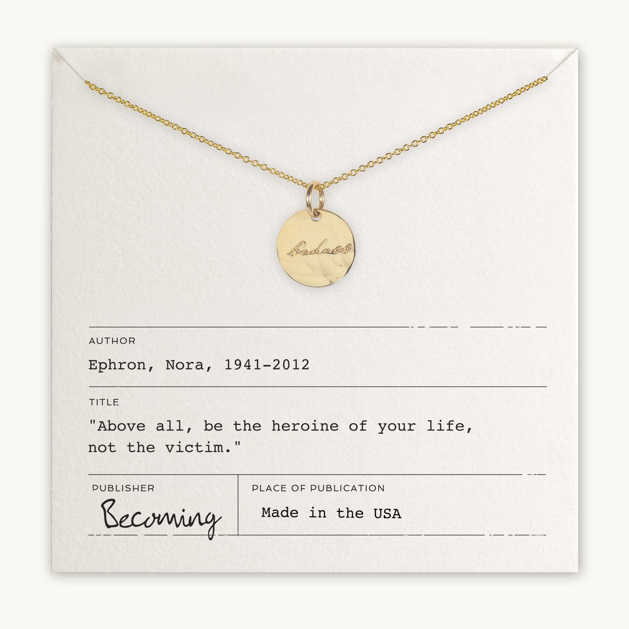 A Badass Necklace by Becoming Jewelry with the word &quot;becoming&quot; engraved, displayed on a card featuring a quote by Nora Ephron, &quot;Above all, be the heroine of your life, not the victim&quot;.