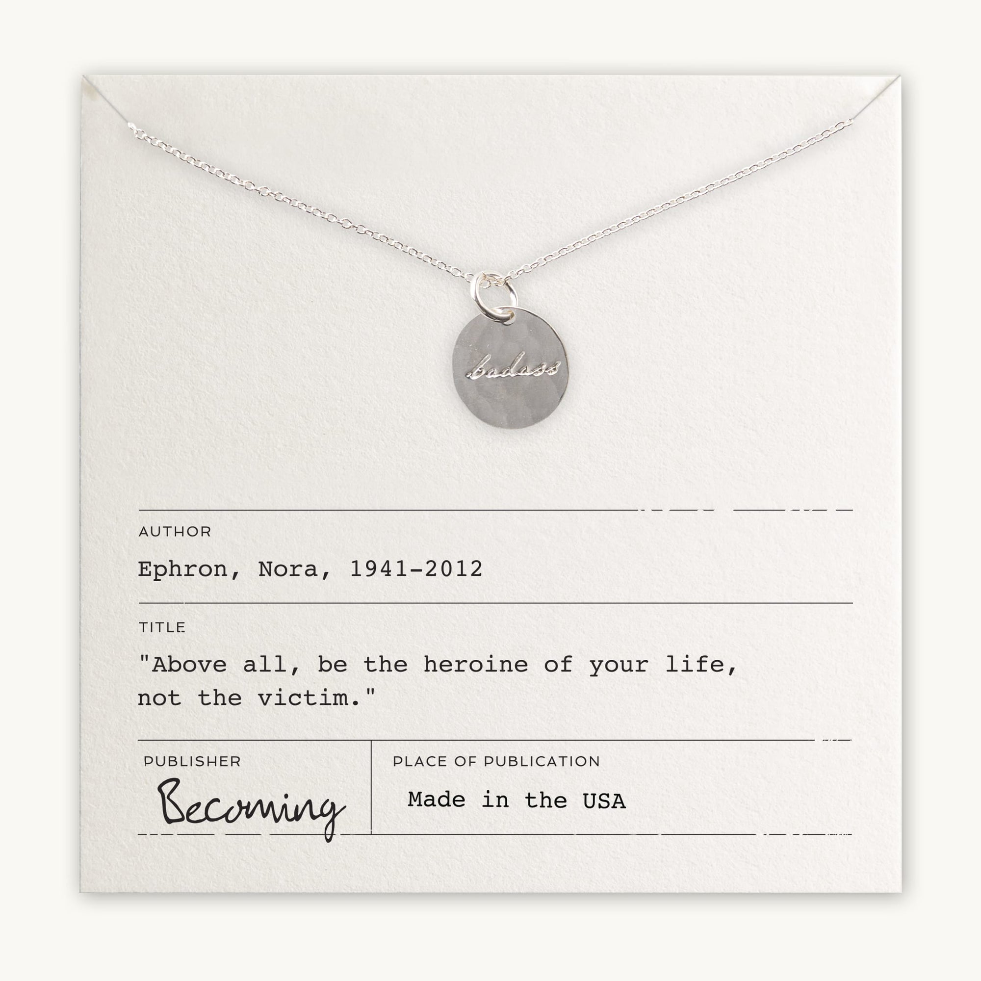 Becoming Jewelry&#39;s Badass Necklace features a gold filled charm with &quot;badass&quot; inscription on a card featuring a quote by Nora Ephron.