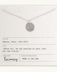 The "Badass Necklace" by Becoming Jewelry showcases a silver necklace with a round pendant inscribed with "badass," elegantly displayed on a card adorned with an antique handwriting font and featuring an inspiring quote by Nora Ephron: "Above all, be the heroine of your life, not the victim." This piece exudes empowerment and elegance.