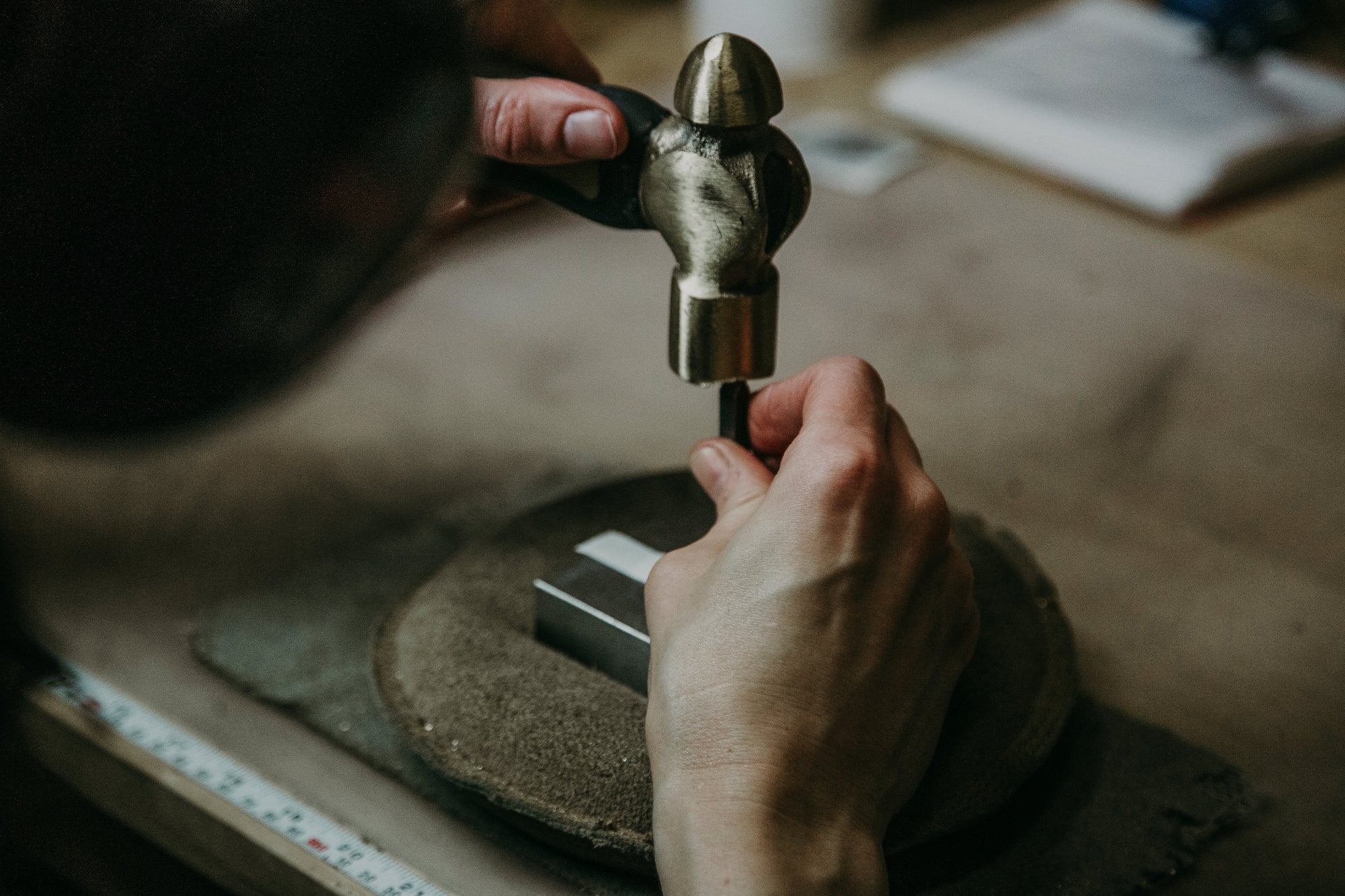 Hands holding a metal rod while using a hammer to shape or work with the rod on a workbench.
