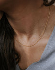 A person wearing a Becoming Jewelry Figaro Chain Necklace and a gray V-neck shirt.