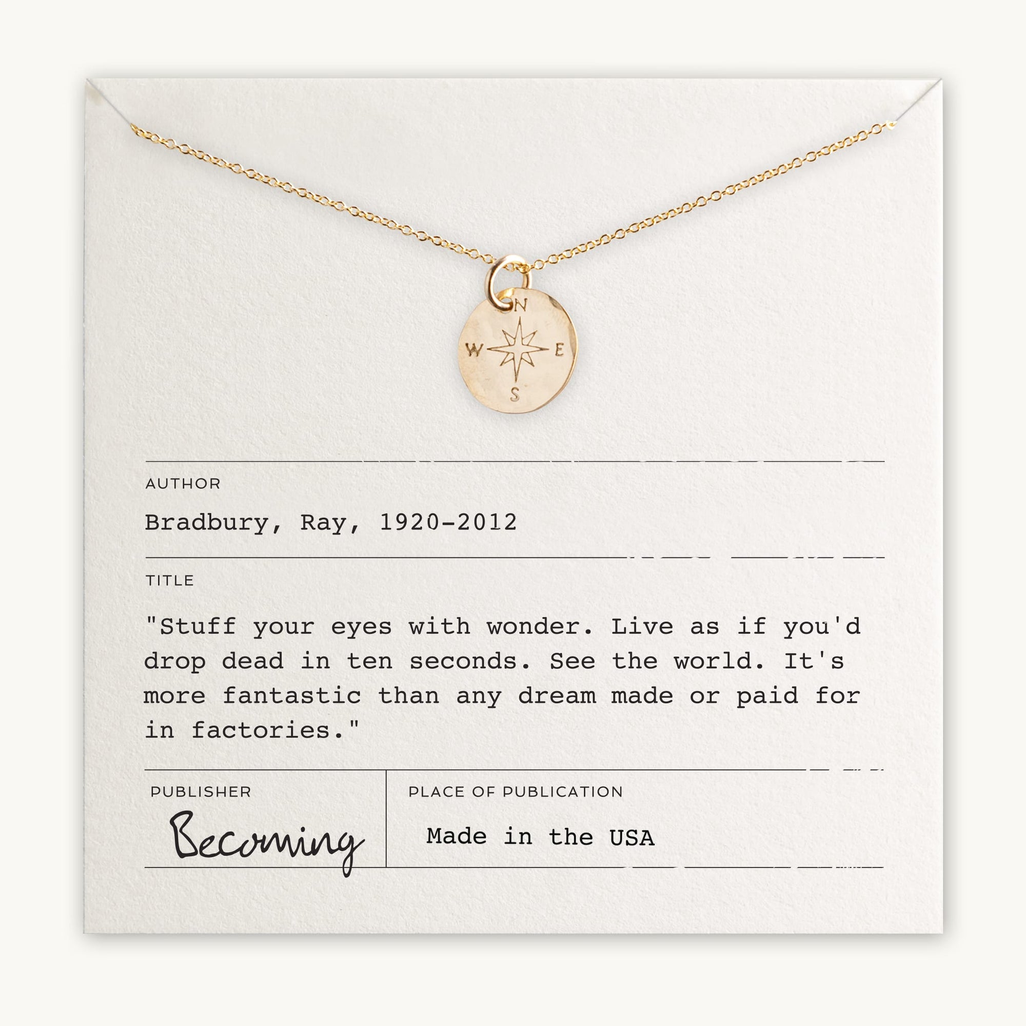 A gold Compass Necklace by Becoming Jewelry is displayed on a card that features an inspiring quote attributed to Ray Bradbury, encouraging wonder and travel. The card is labeled "Becoming," making this an ideal motivational gift, and it proudly states "Made in the USA.