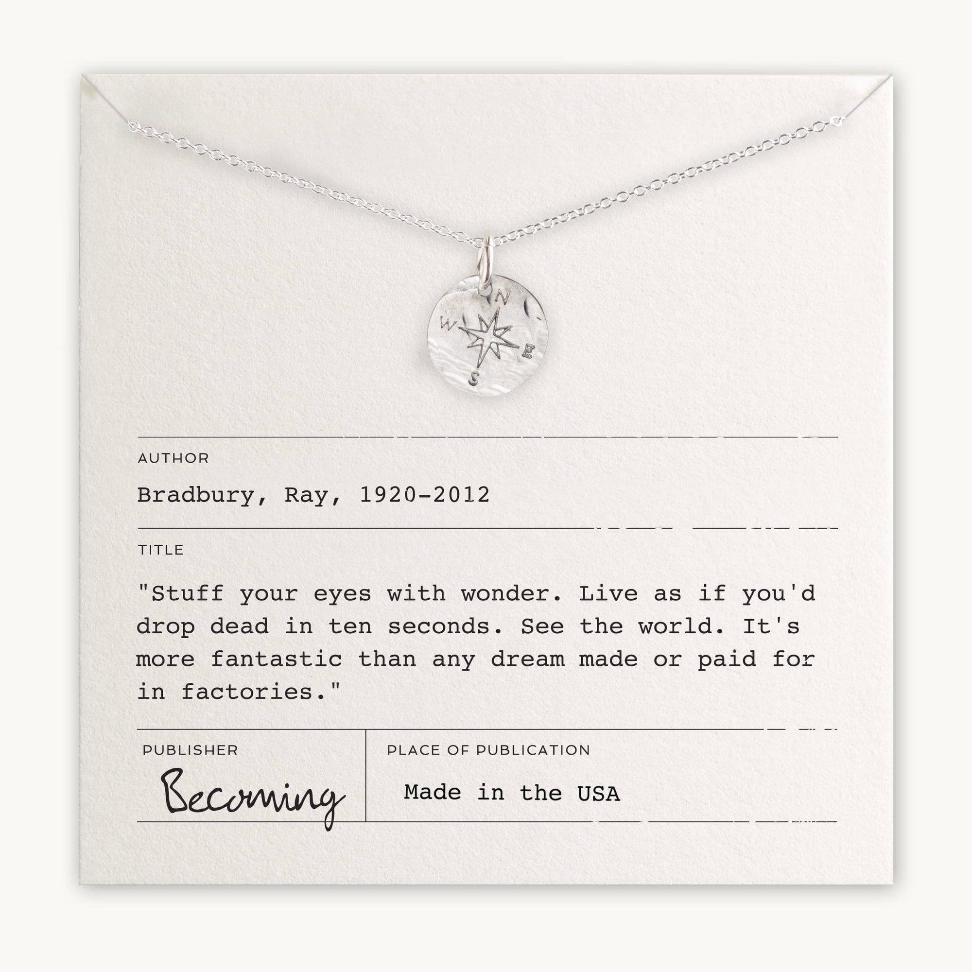A silver Compass Necklace by Becoming Jewelry is displayed on a card featuring a quote from Ray Bradbury's "Becoming," which reads, "Live as if you'd drop dead in ten seconds." Ideal for travel inspiration, the card also includes information about the author, title, publisher, and origin.