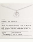 A silver Compass Necklace by Becoming Jewelry is displayed on a card featuring a quote from Ray Bradbury's "Becoming," which reads, "Live as if you'd drop dead in ten seconds." Ideal for travel inspiration, the card also includes information about the author, title, publisher, and origin.
